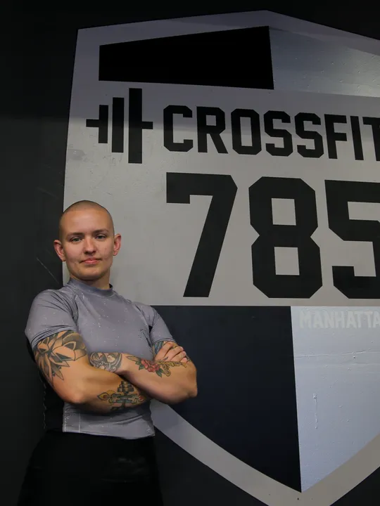 Coach Annie, arms folded and smiling, in front of the CrossFit 785 wall at the gym.