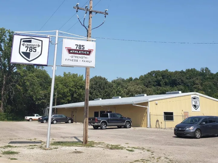The gym from the road: two signs reading CrossFit 785 and 785 Athletics, in front of a yellow metal building with a gravel parking lot.