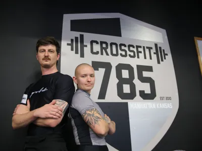 Coach Hunter and Coach Annie standing back to back in front of the CrossFit 785 wall.