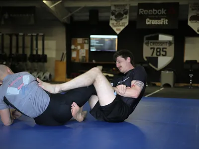 Two members seated on the mat with their legs entangled, working for position.