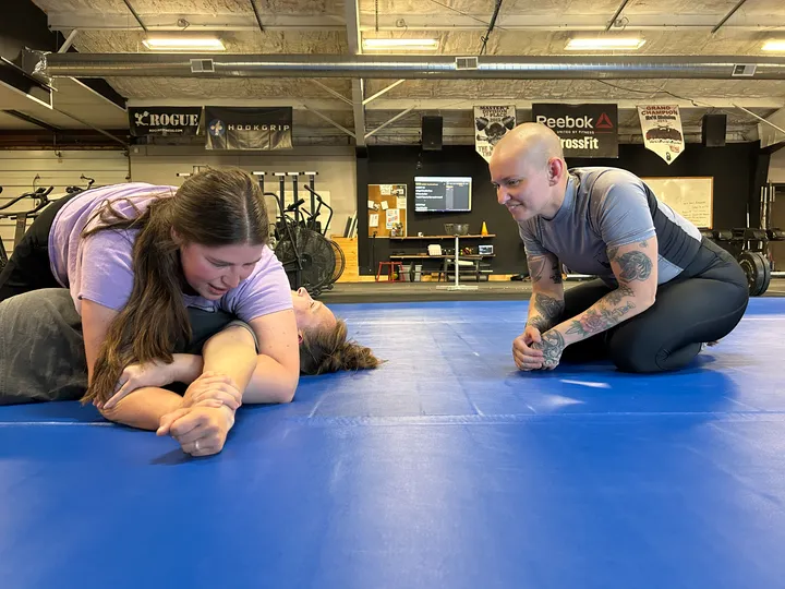 Coach Annie kneeling beside two members and talking them through a position during the Women&rsquo;s BJJ class.